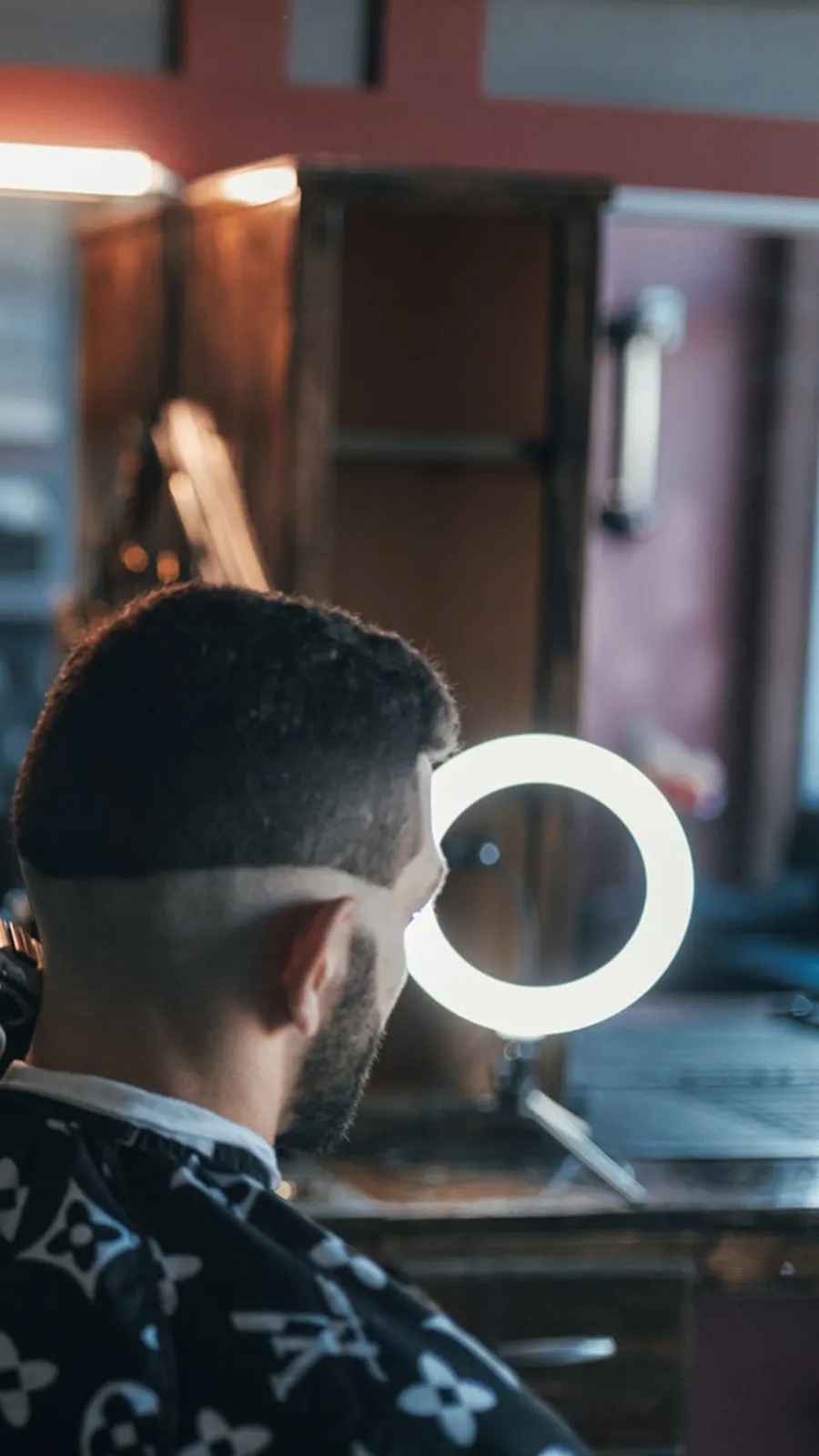 Cliente de costas, em frente a um espelho redondo com luz